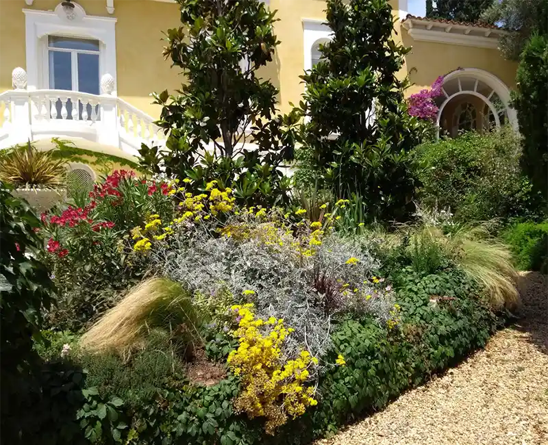 Jardín mediterráneo en flor frente a una casa con balaustrada